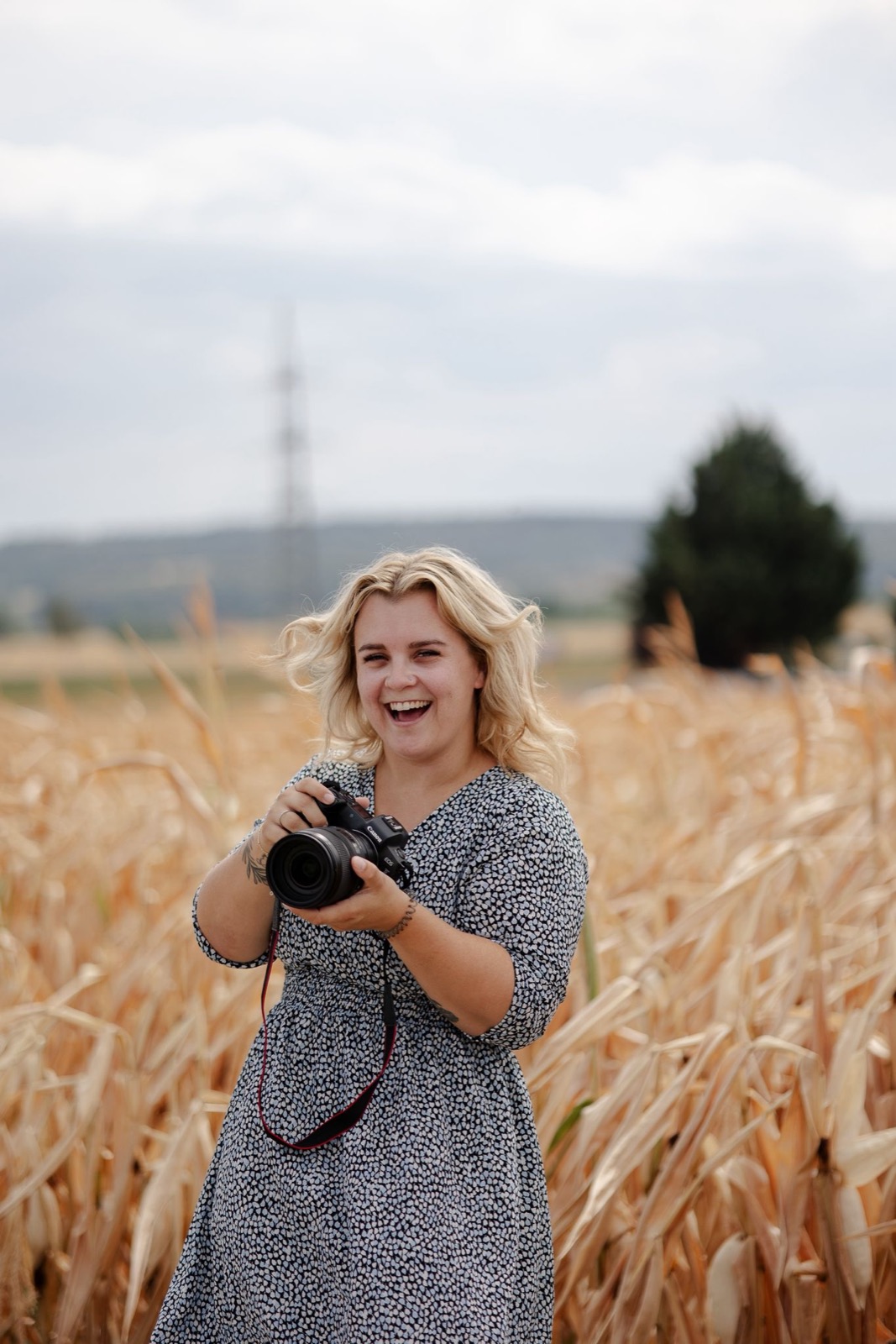Stefanie Exeli lachend mit Kamera in einem Kornfeld